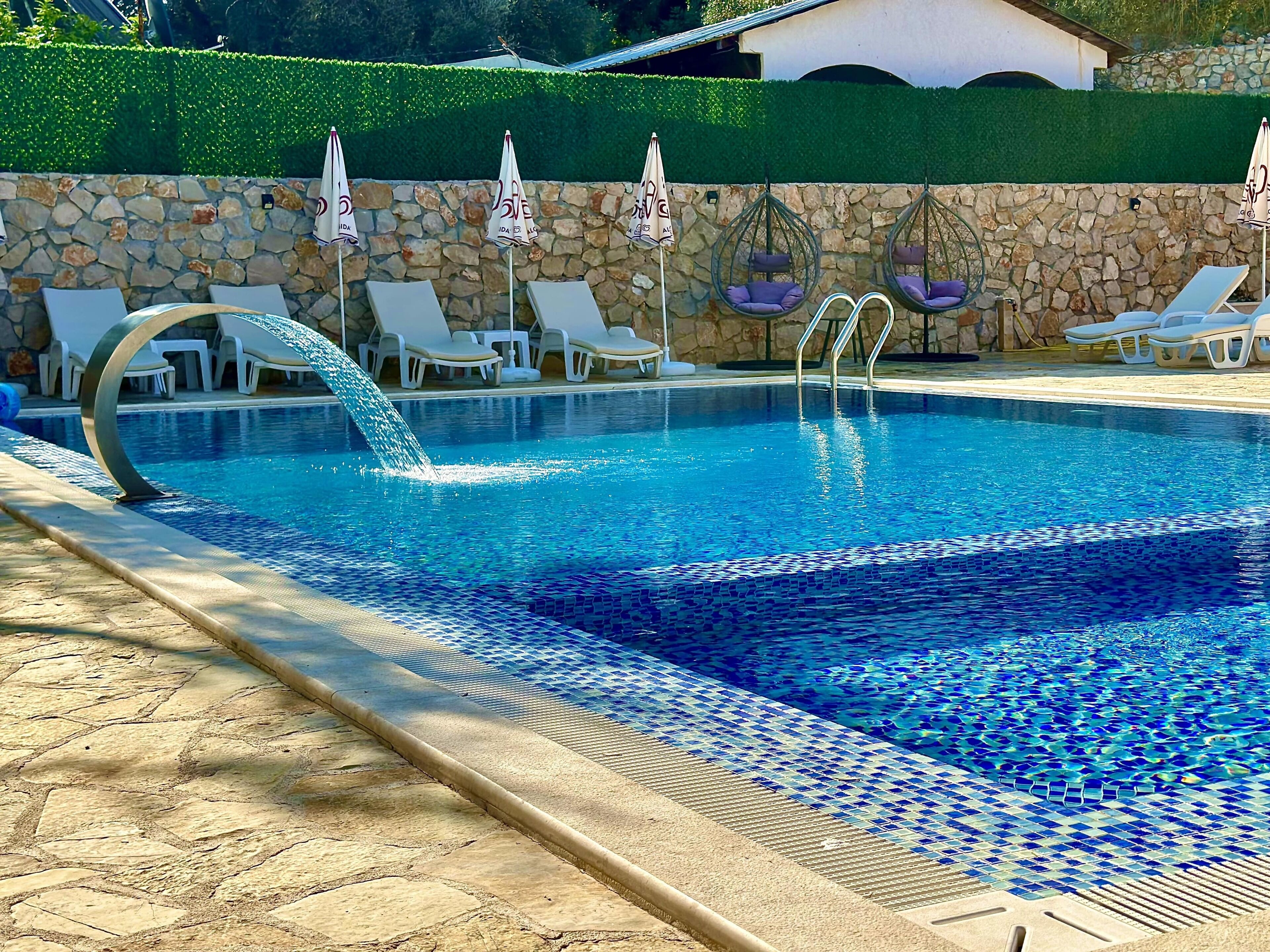 Una piscina amb mur de pedra i cadiretes penjades.
