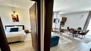 A modern hotel room with a bed, a desk, and a dining area. - Akhdar Apartments (Utjeha)