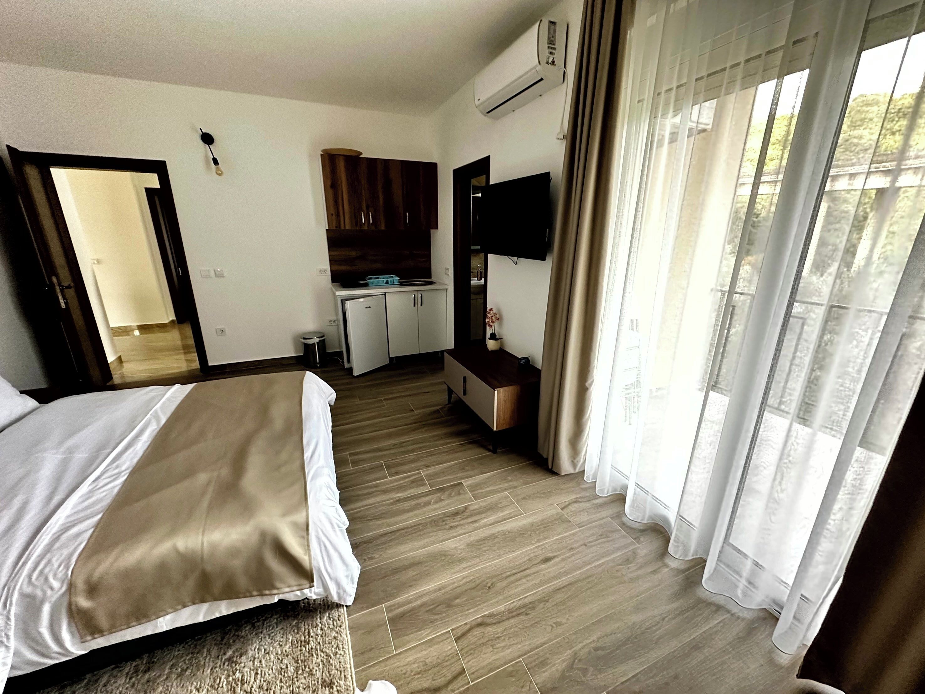 Una camera d'albergo con un letto, un angolo cottura, una TV e una finestra con tende.