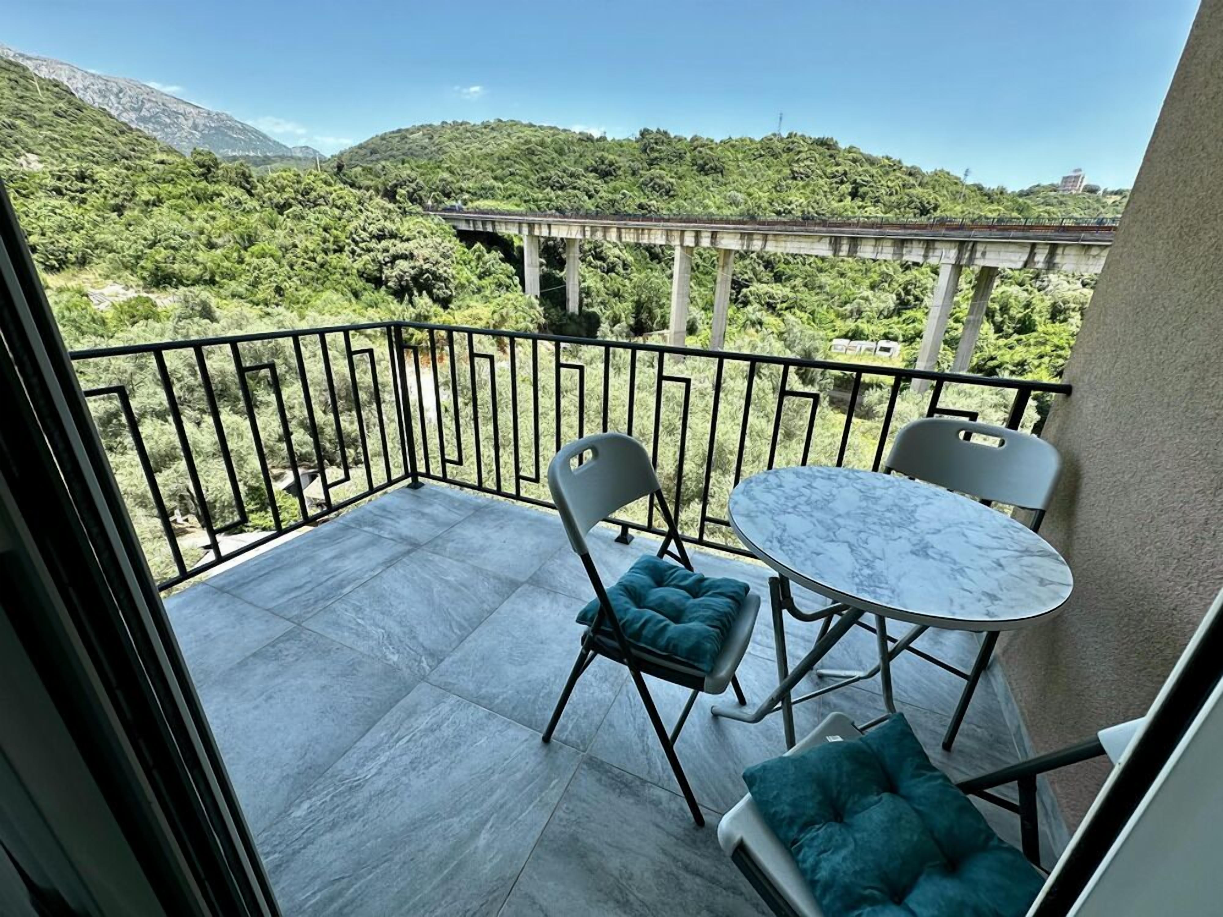 A balcony with a marble table and chairs, a view of a bridge and greenery.