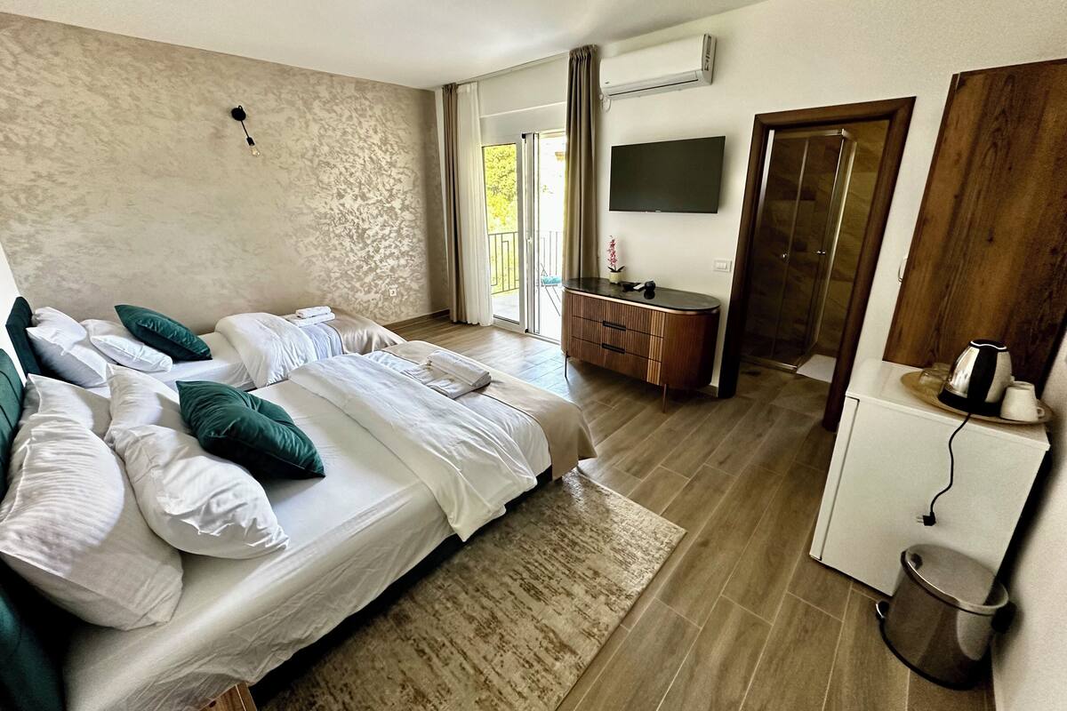 A modern hotel room with a large bed, a flat-screen TV, a wooden cabinet, and a small kitchenette.