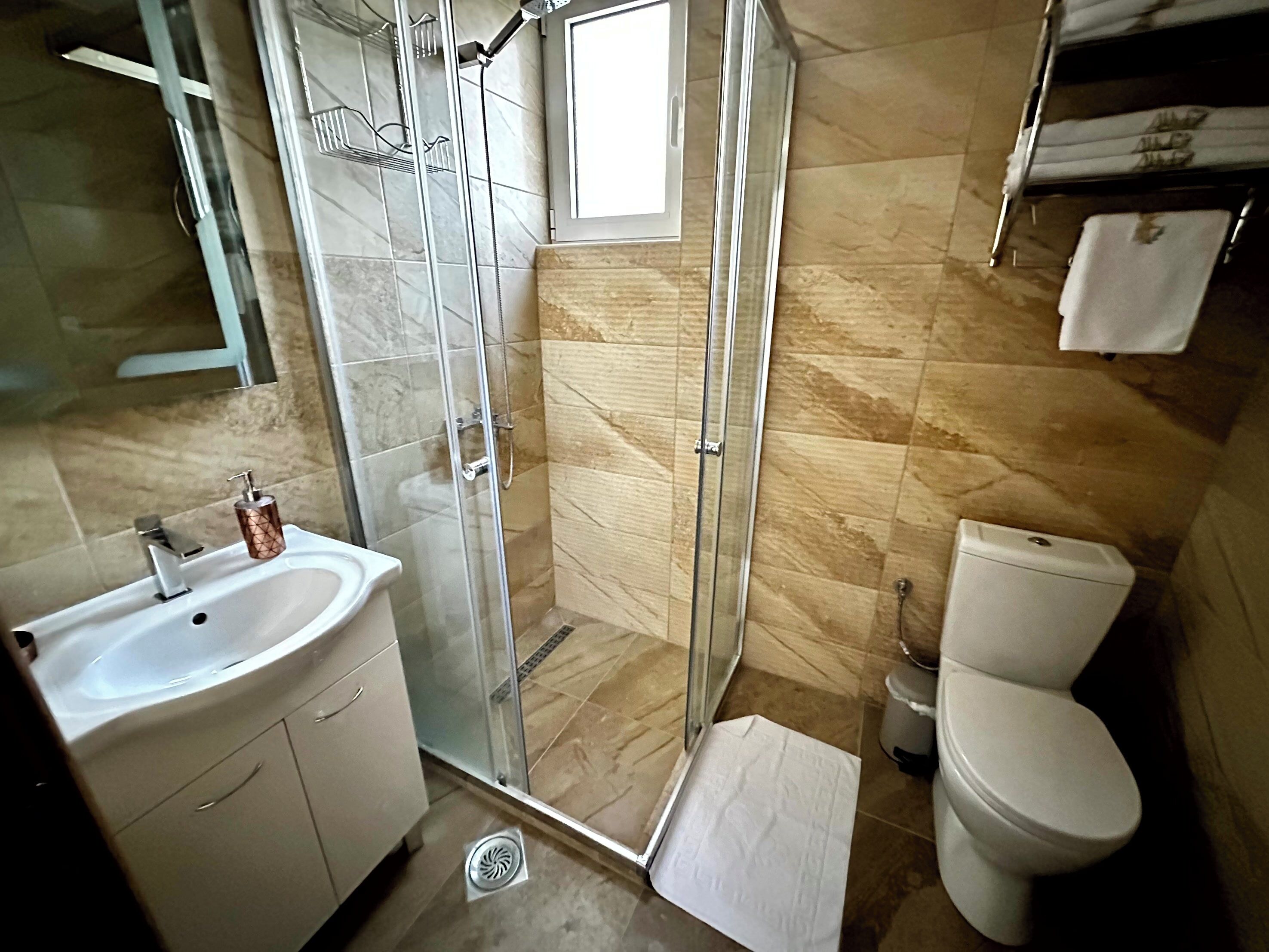 Une salle de bain avec une douche à parois de verre, un lavabo, des toilettes et une petite fenêtre.