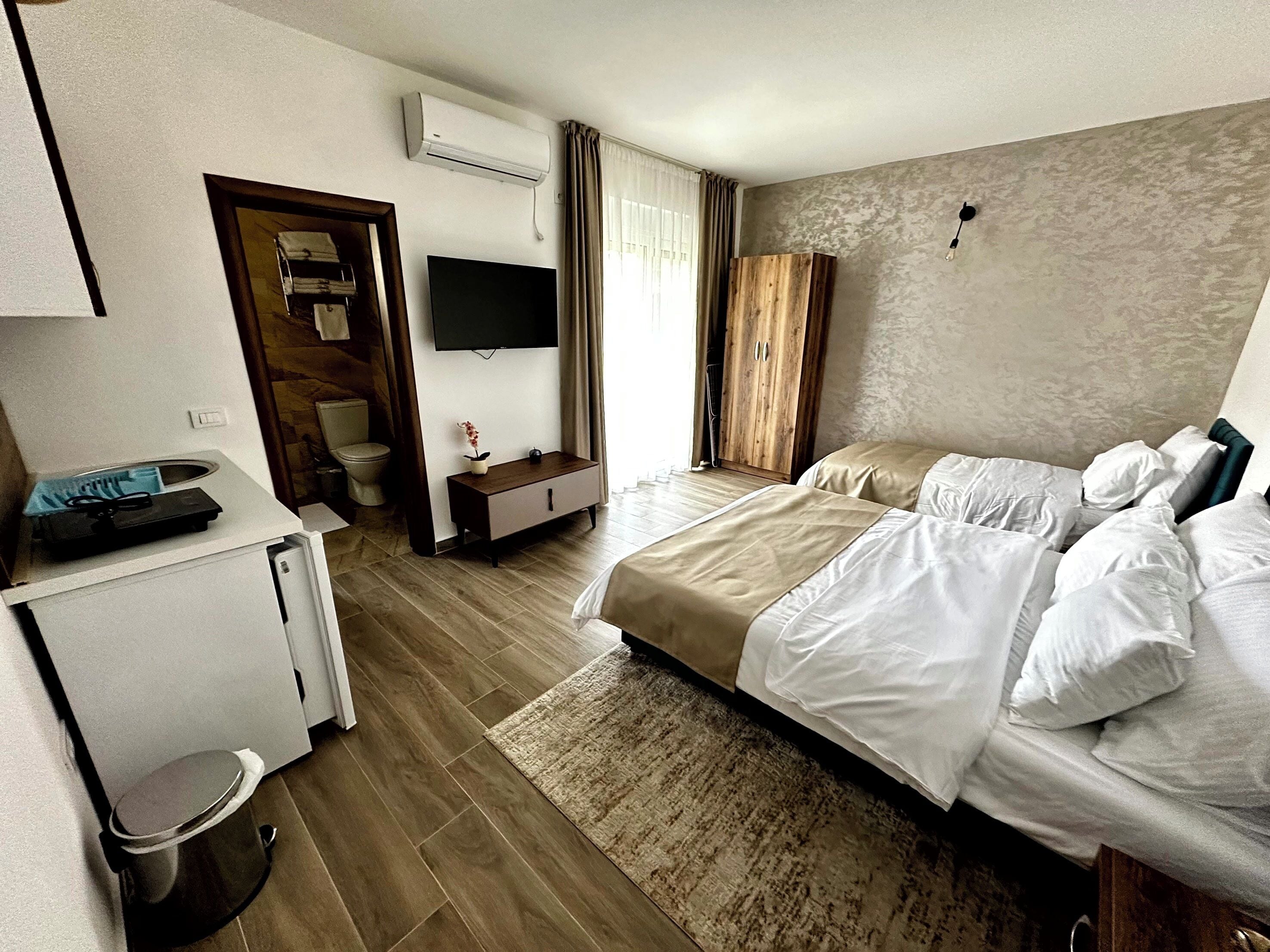 Ein Hotelzimmer mit einem Bett, einem Fernseher, einem Kleiderschrank, einem kleinen Schreibtisch mit Computer und einem Mülleimer.