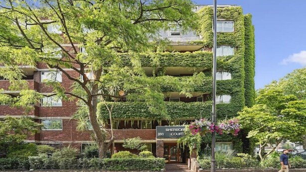 En byggnad med flera våningar, en fasad av tegel och gröna klätterväxter. Ett skylt säger ”Sherwood Court”.
