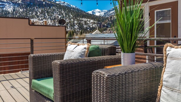 Sillones de mimbre con cojines en una terraza con vistas a una montaña nevada.