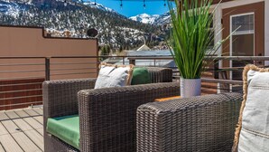 Cadeiras de vime com almofadas em um deck com vista para uma montanha coberta de neve.