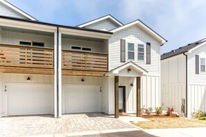 A two-story residential building with a garage, a covered porch, and a small garden area.