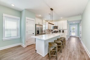A modern kitchen with a central island, stainless steel appliances, and wooden bar stools. - Wave After Wave | Dogs OK, Walk to Beach, Pool (Corolla)
