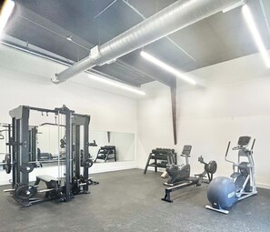 A gym with various exercise equipment, including a squat rack, dumbbells, and an elliptical machine.