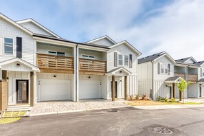 A row of townhouses with attached garages, a paved driveway, and a clear sky. - Wave After Wave | Dogs OK, Walk to Beach, Pool (Corolla)
