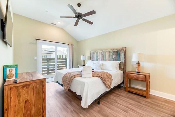 A bedroom with a bed, bedside tables, a ceiling fan, and a view through a sliding door.