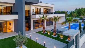 A modern multi-story house with a swimming pool, outdoor seating, and well-maintained landscaping.
