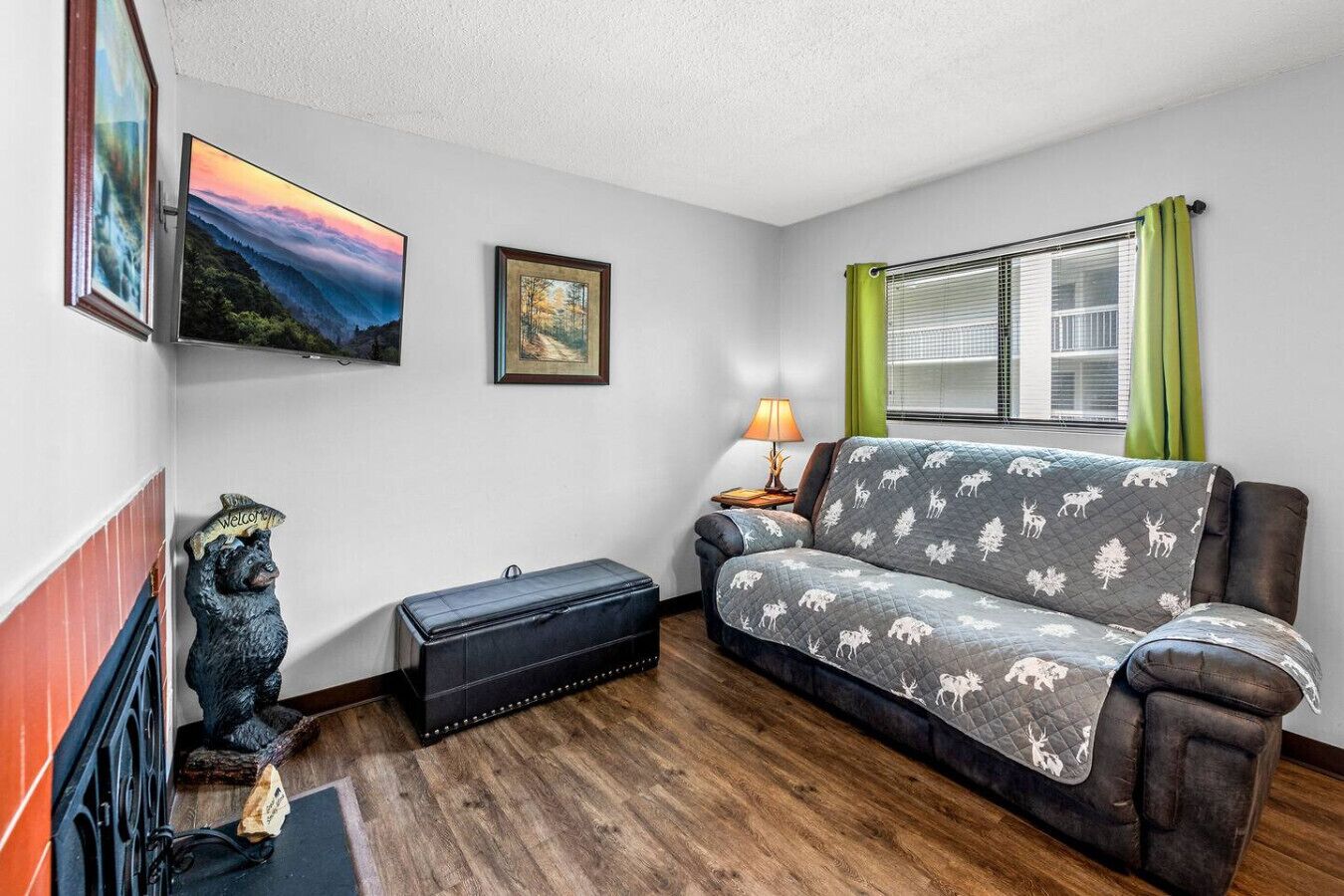 Ein Wohnzimmer mit Sofa, Lampe, einer Bärenstatue, einem Koffer und einem Bild an der Wand.