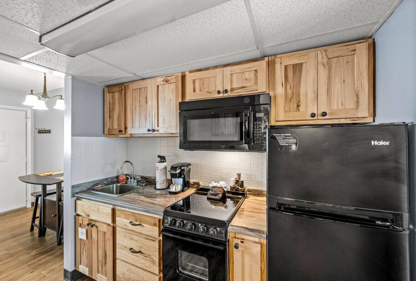Une cuisine avec des meubles de rangement en bois, un réfrigérateur noir, une cuisinière et un four à micro-ondes.