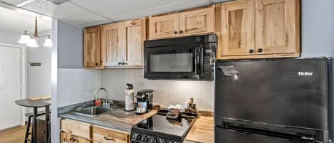 Une cuisine avec des meubles de rangement en bois, un réfrigérateur noir, une cuisinière et un four à micro-ondes.
