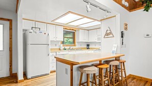 A modern kitchen with white cabinets, a wooden island with stools, a skylight, and a wooden ceiling. - New! Private 2BR Cabin w/Hot Tub*Central Location (Sevierville)