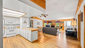 A spacious living area with a fireplace, wooden flooring, and a kitchen with white cabinetry and a microwave. - New! Private 2BR Cabin w/Hot Tub*Central Location (Sevierville)