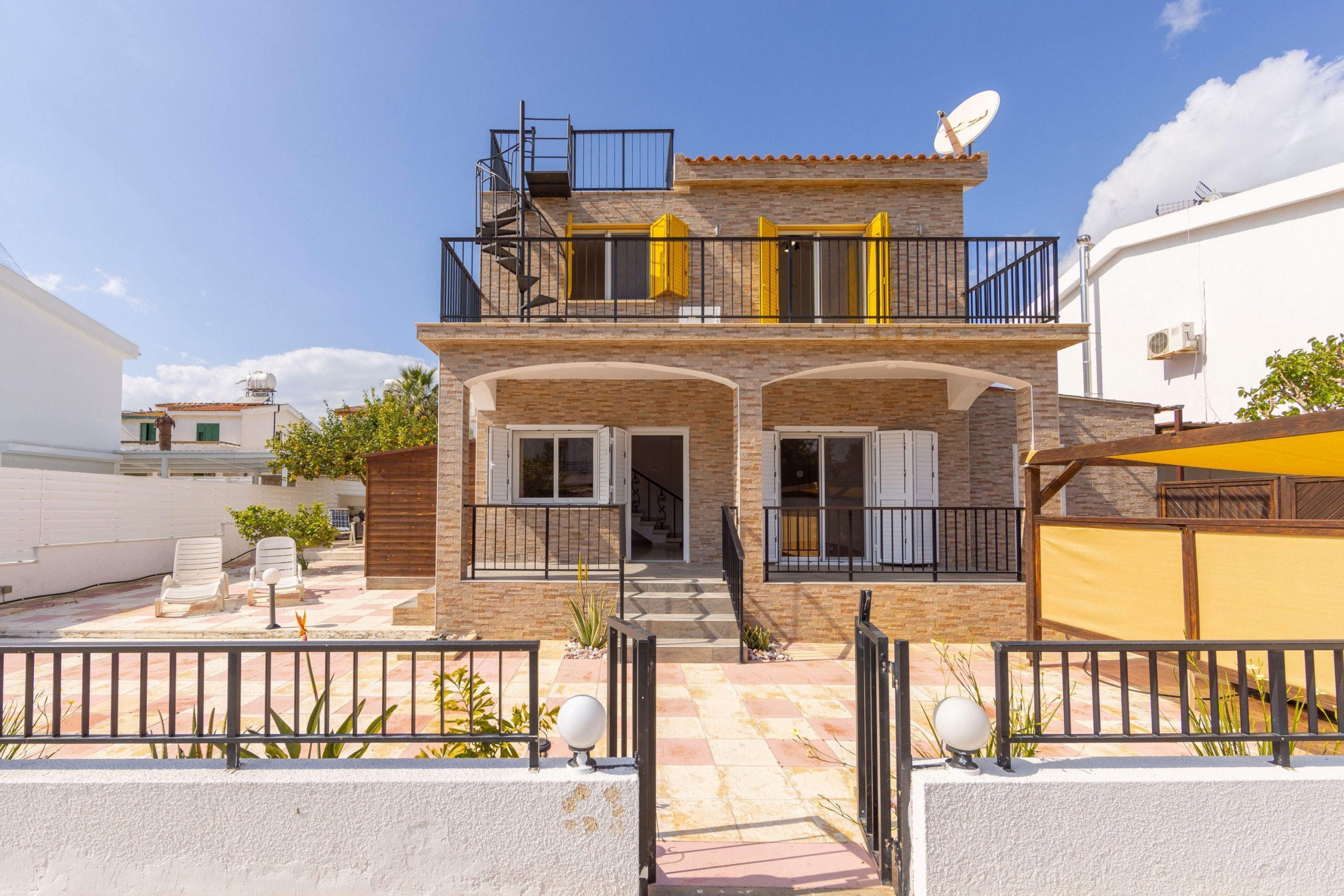 A two-story house with a balcony, a satellite dish, and a small patio area with chairs.