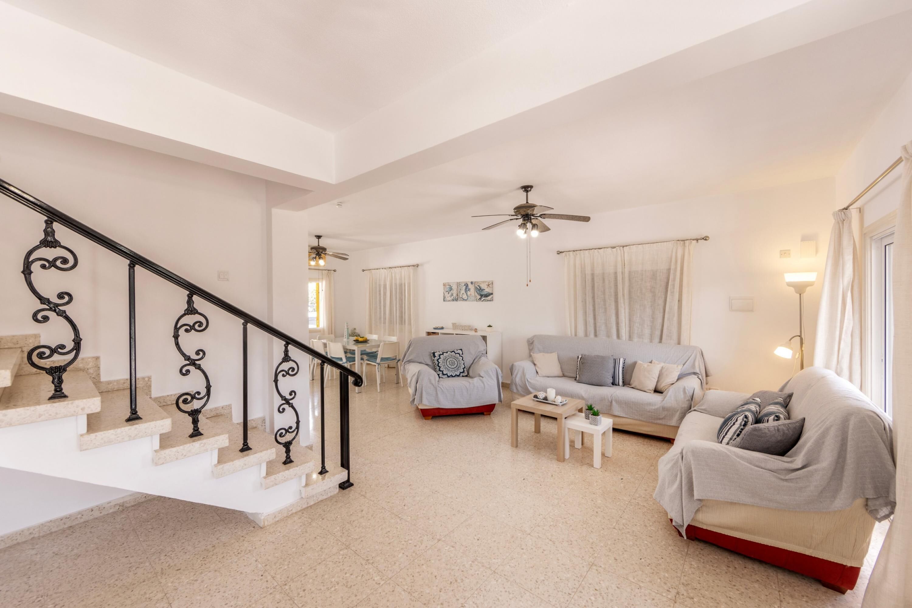 Ein geräumiger Wohnbereich mit Treppe, Sofa, Couchtisch und Deckenventilator.
