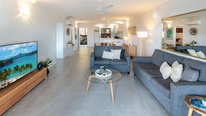 A modern living room with a TV, sofas, a coffee table, and a kitchen in the background.