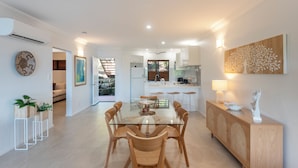 A modern kitchen with white cabinets, a central island, and a dining area with a glass table and wooden chairs.