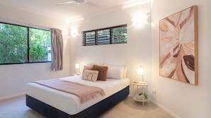 A bedroom with a bed, bedside tables, a window with curtains, a wall-mounted artwork, and a ceiling fan.