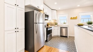 Una cocina moderna con armarios blancos, electrodomésticos de acero inoxidable, piso estampado y ventana con vistas.