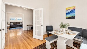 Un comedor con una mesa blanca, sillas grises y un banco. Hay un cuadro en la pared y una planta en la mesa.