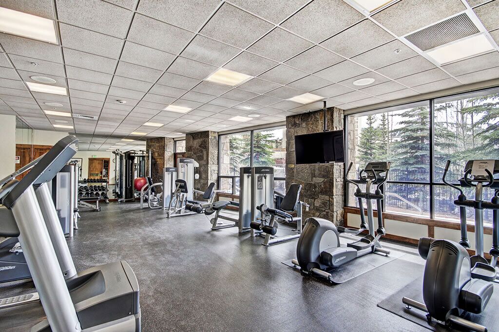 Un gimnasio con cintas de correr, máquinas de pesas y un amplio ventanal con vistas a árboles.