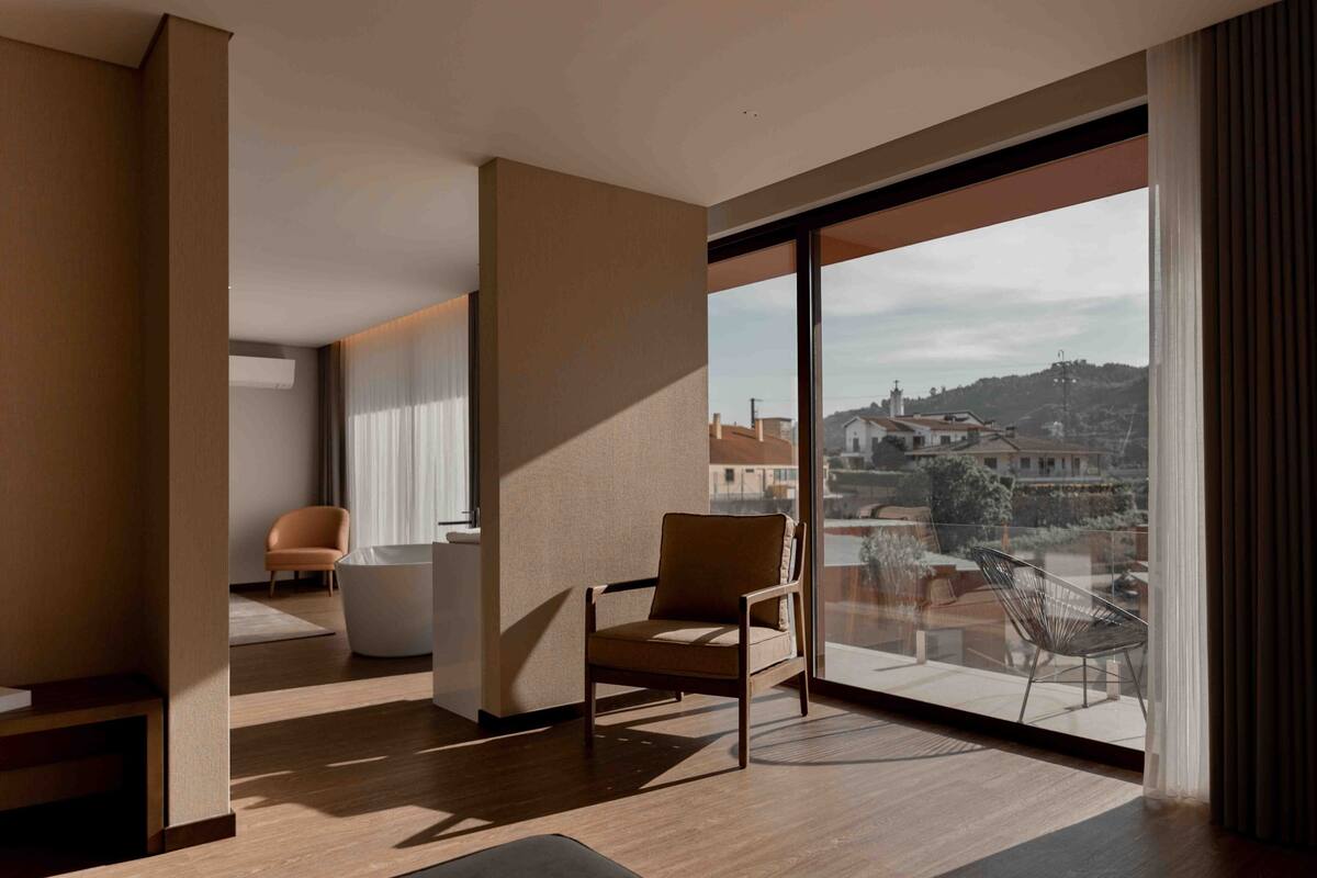 A modern room with a large sliding glass door leading to a balcony, a wooden floor, a sofa, and a chair.
