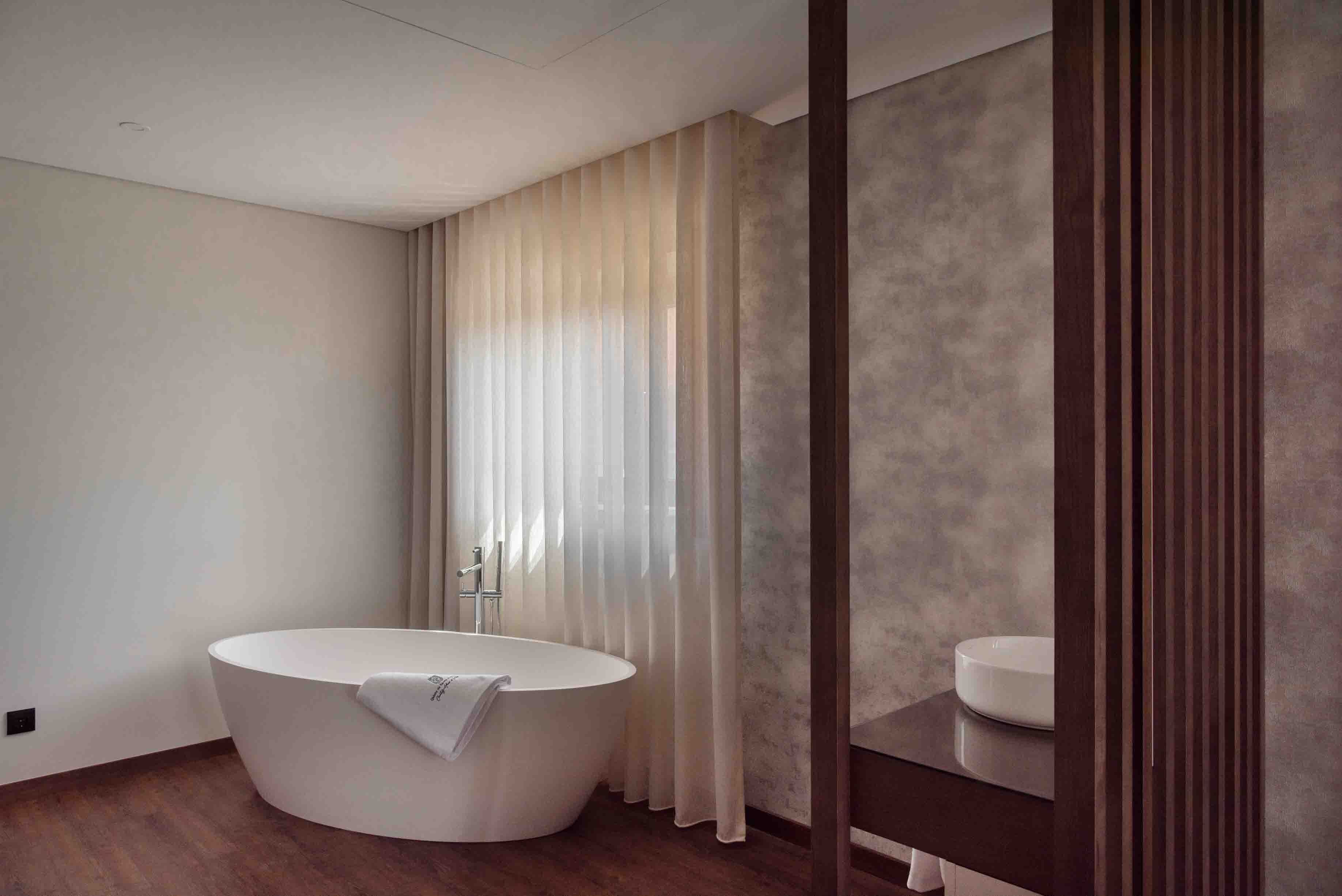 A modern bathroom with a freestanding bathtub, a vanity with a mirror, and a large window with curtains.
