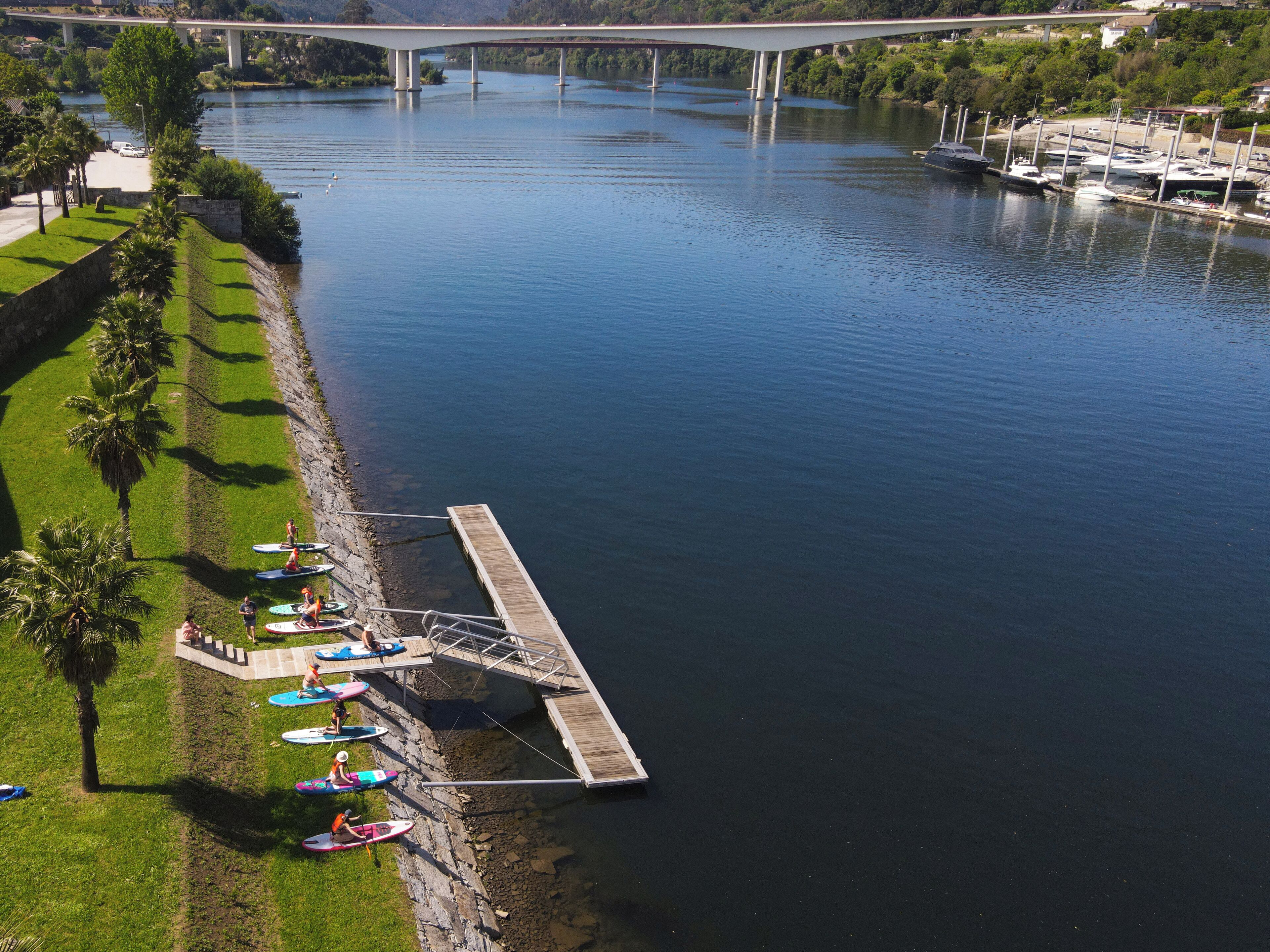 A riverside dock with paddleboards, a bridge in the background, and a marina with boats.