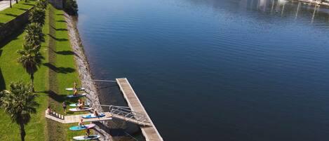 A riverside dock with paddleboards, a bridge in the background, and a marina with boats.