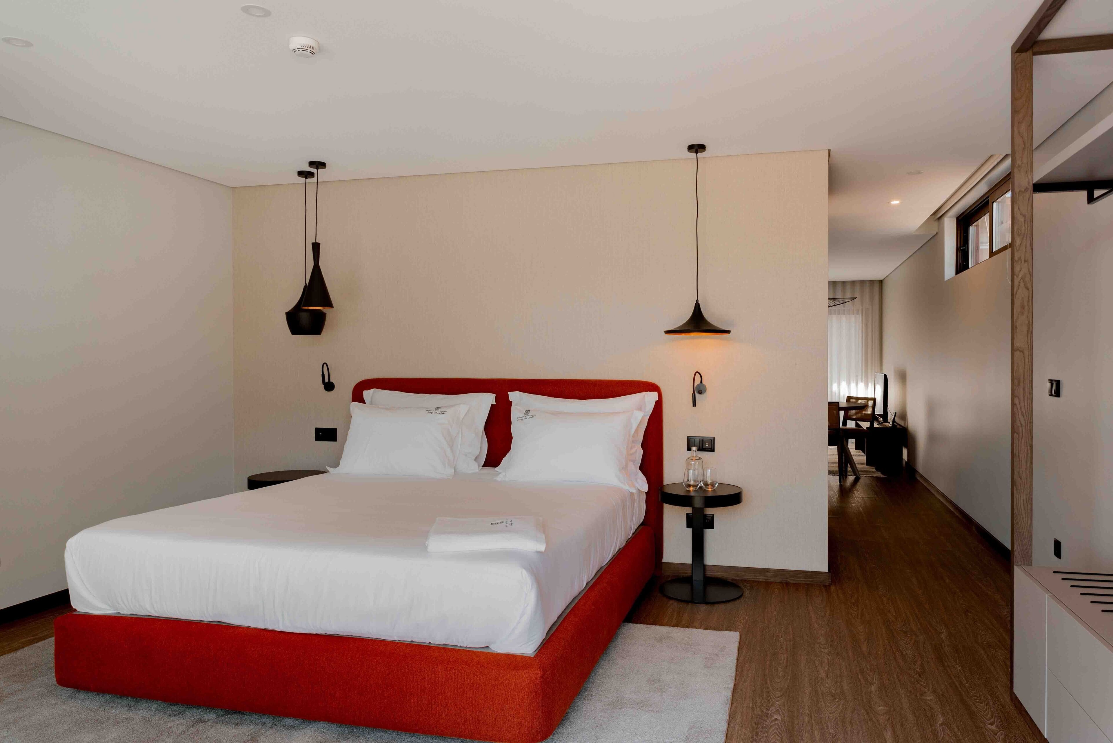 Een moderne hotelkamer met een rood bed, witte beddengoed en twee hanglampen.