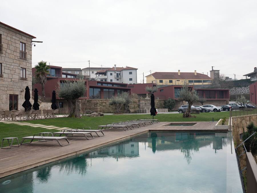 A swimming pool with lounge chairs, a stone building, and a parking area with cars.