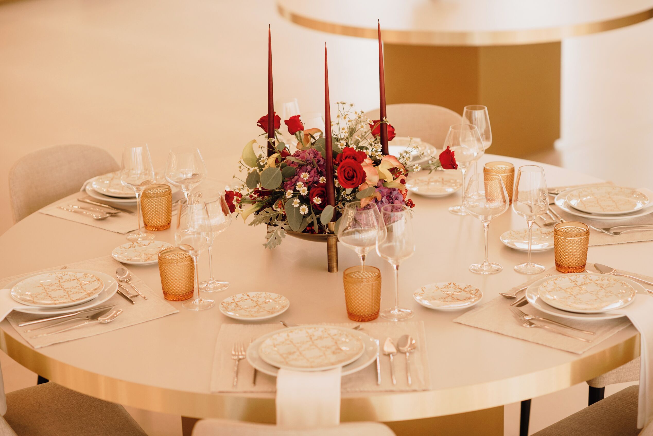 A round dining table set for a meal with plates, cutlery, and glassware.