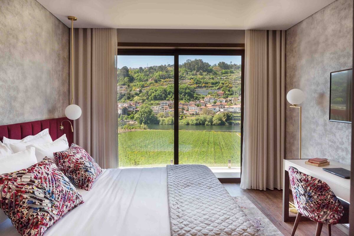 A hotel room with a large bed, a desk, and a view of a hillside town.
