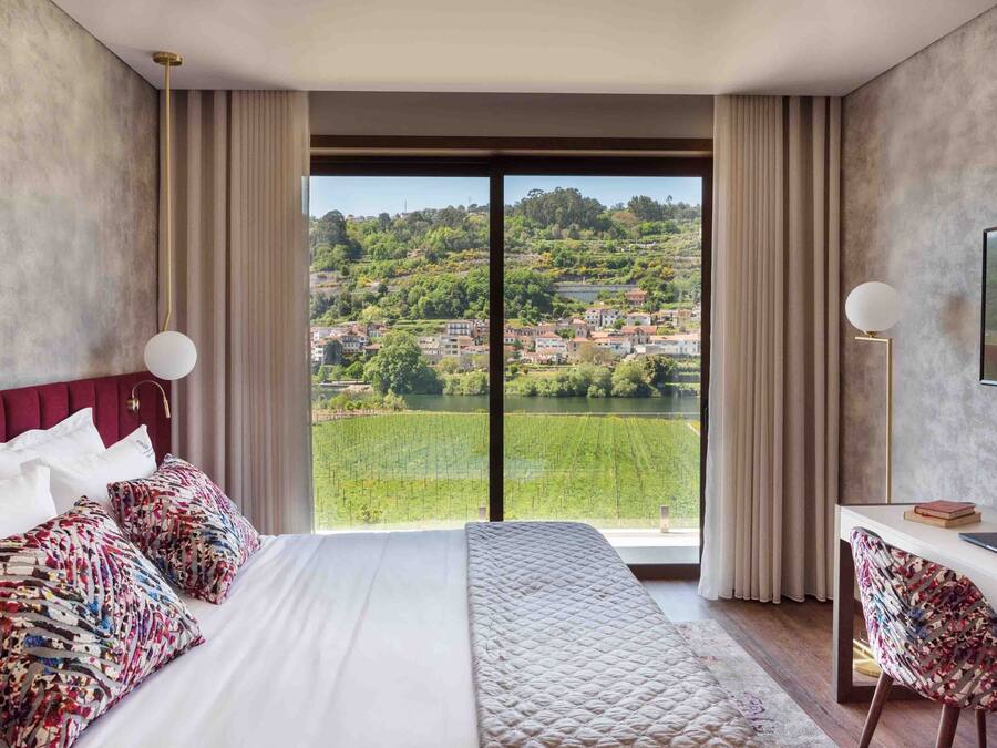 Habitació d'hotel amb un llit gran, un escriptori i vista a un poble situat a la vora d'una collada.
