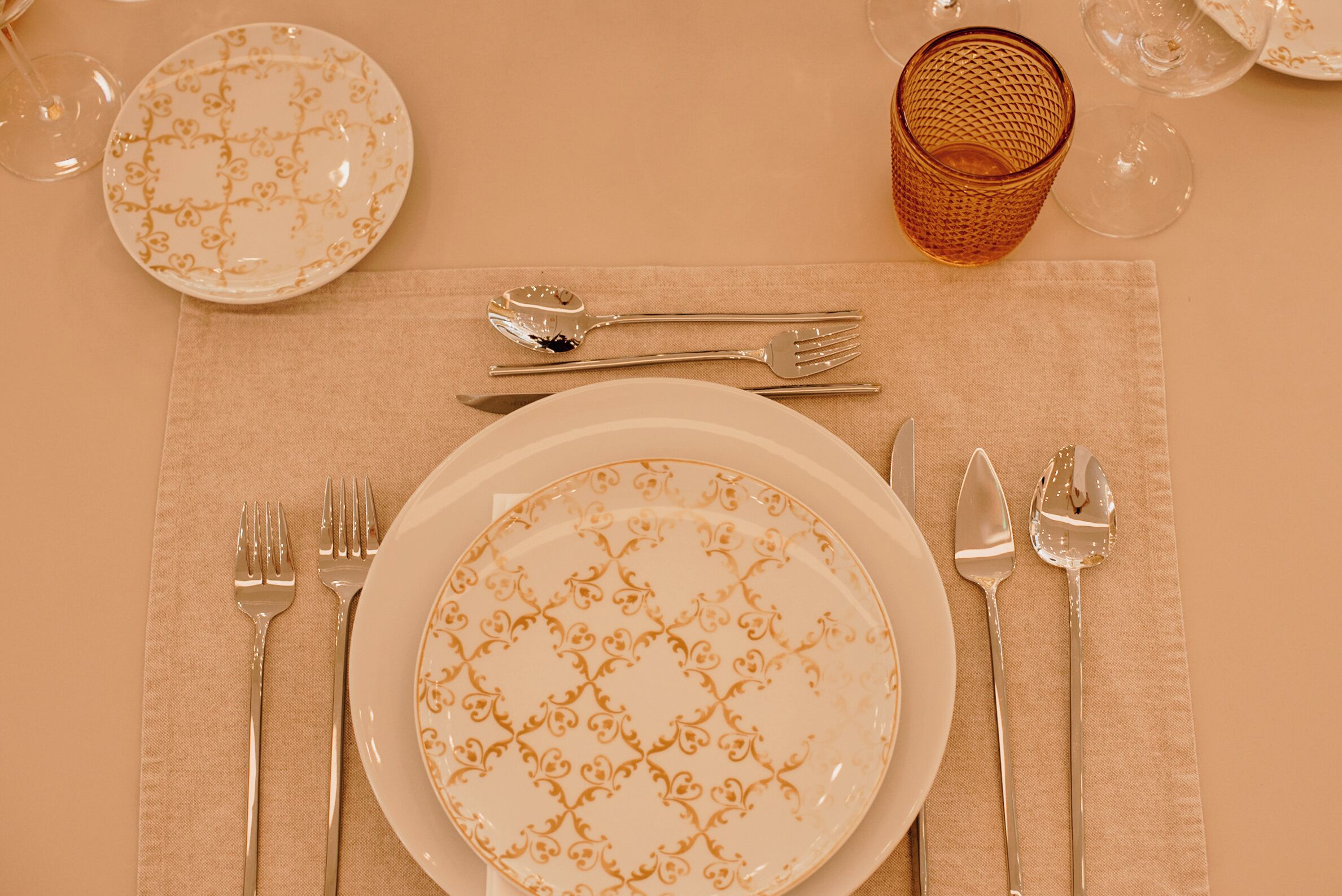 Una mesa dispuesta con platos, cubiertos y vasos, sobre un mantel color beige.