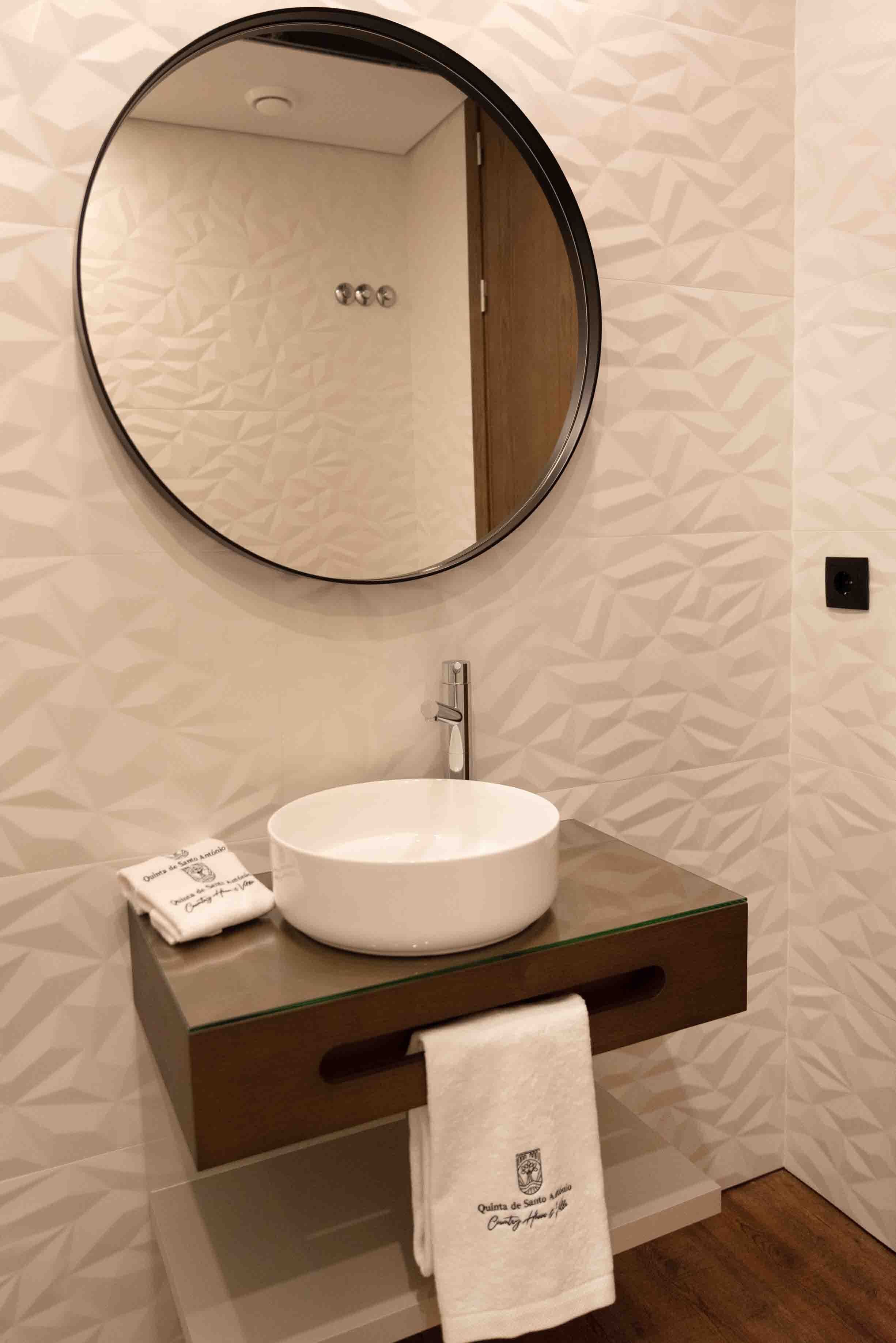 A bathroom with a round mirror, a white sink, and a towel with a logo.
