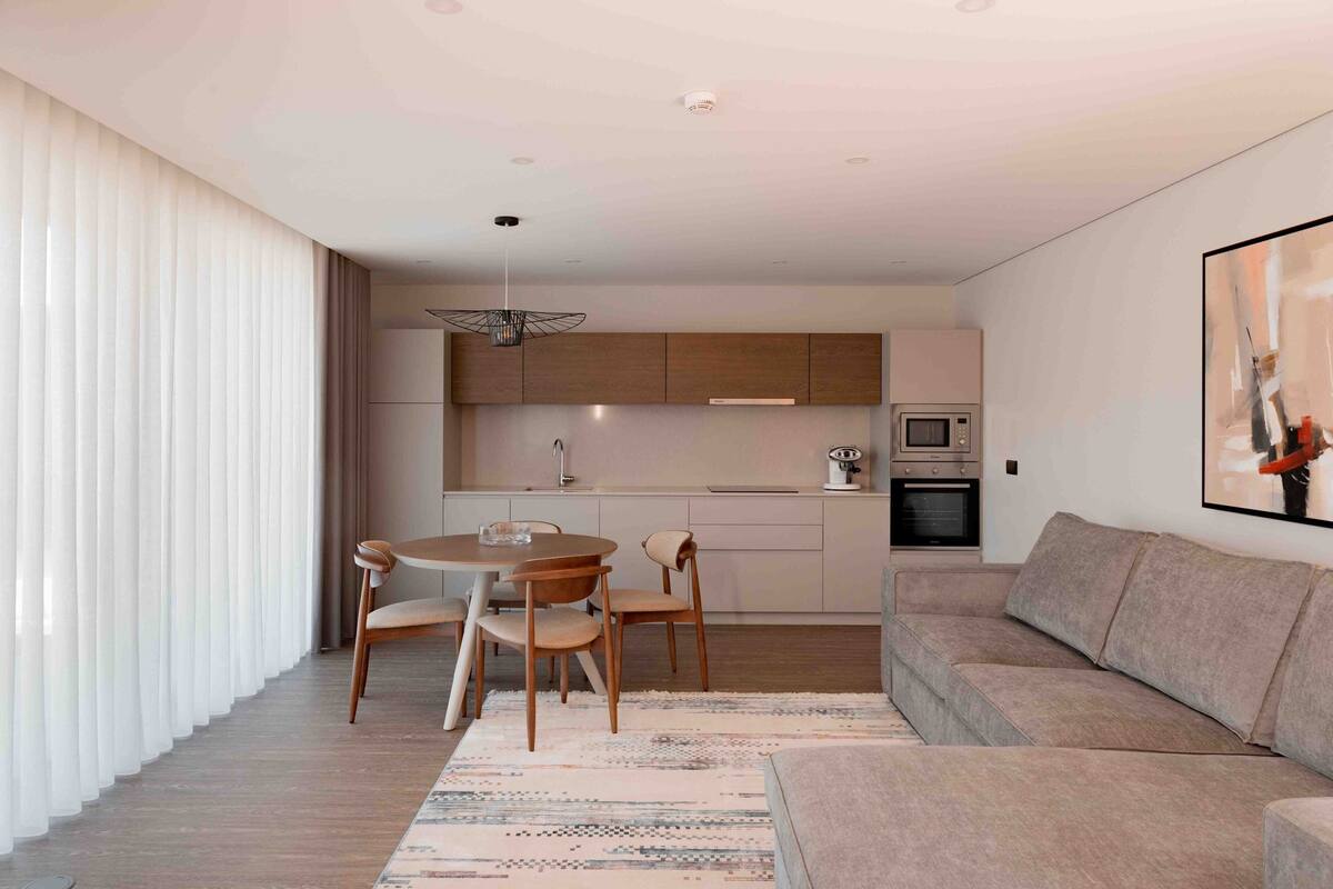 A modern living room with a sofa, a dining table with chairs, and a kitchen area with cabinets and appliances.
