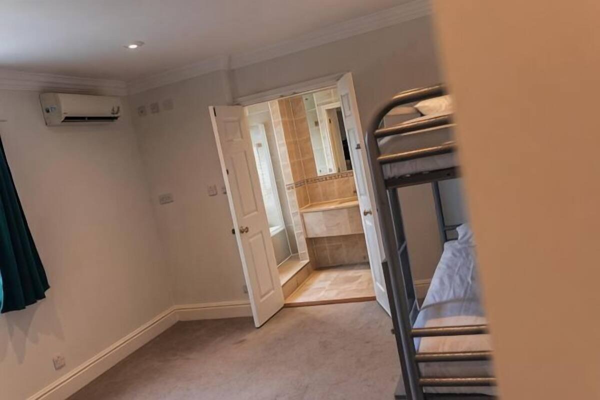 A room with bunk beds, a door leading to a bathroom, and an air conditioning unit on the wall.