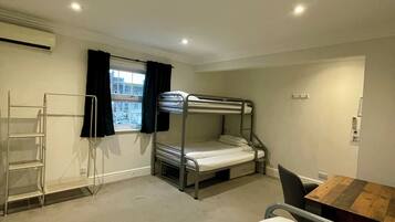 A compact hotel room with bunk beds, a desk, a chair, a ladder, and a window with curtains.