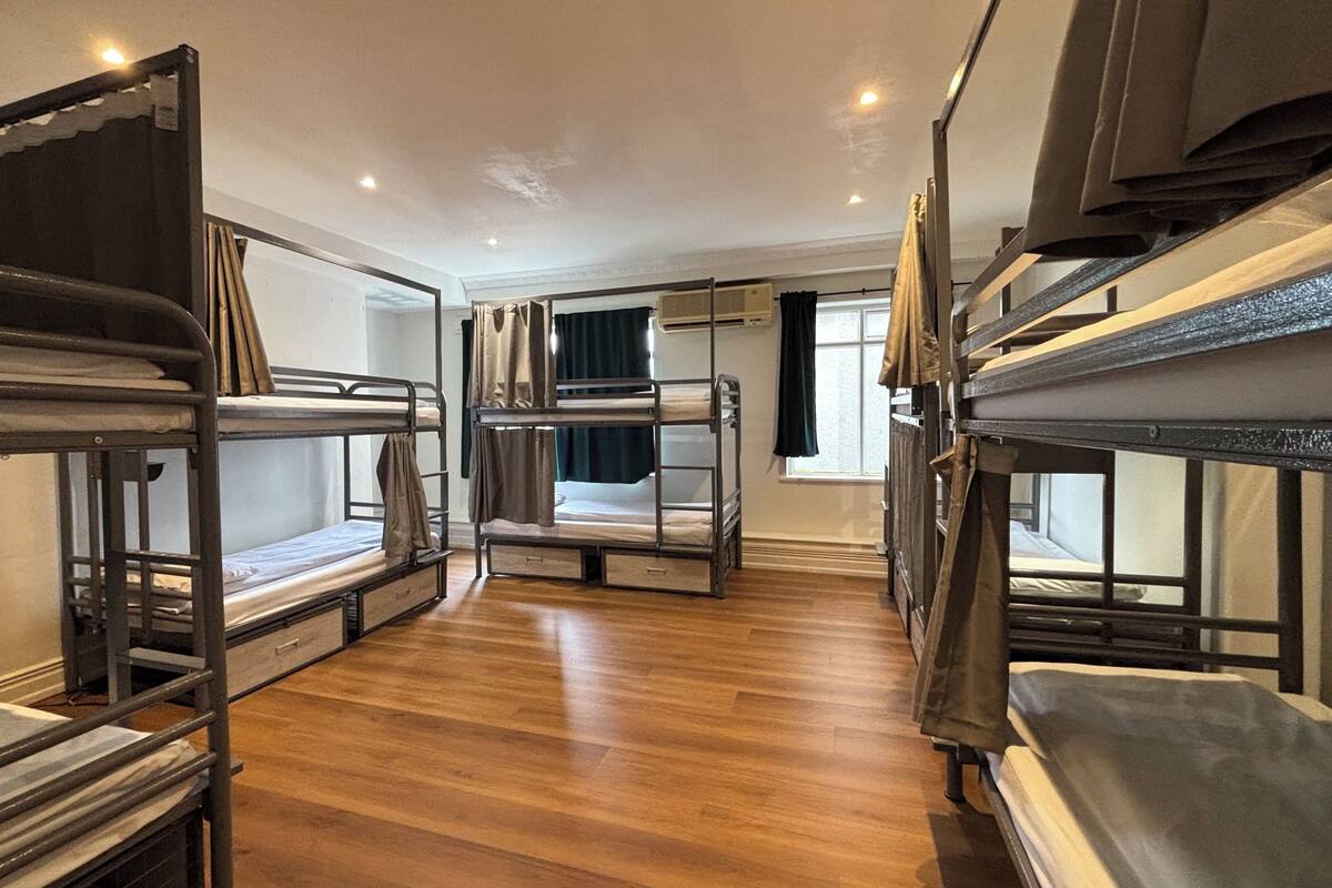 A room with bunk beds, wooden flooring, and a window with curtains.