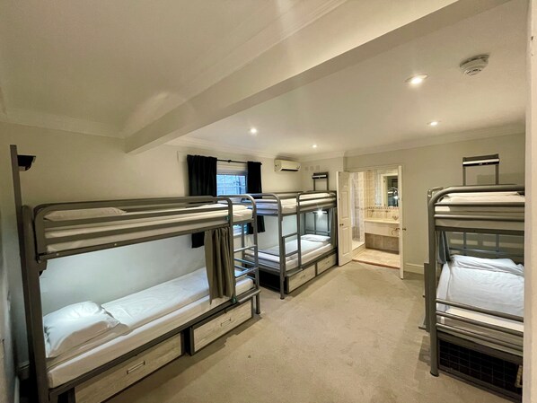 A room with bunk beds, a bathroom with a mirror, and a window with curtains.