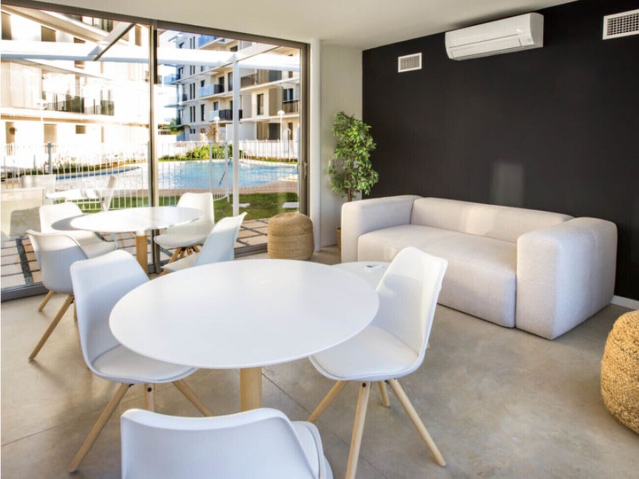 Ein modernes Wohnzimmer mit einem runden Tisch, weißen Stühlen, einer Couch und Blick auf einen Pool sowie Gebäude.