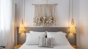 A neatly made bed with white linens and a patterned pillow, flanked by two bedside tables with lamps, and a macramé wall hanging above.