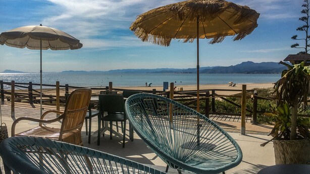 A beachside patio with wicker chairs and umbrellas, overlooking the sea and mountains. - Cullera Beachfront Apartment (Cullera)