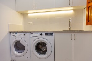 A compact laundry area with two front-loading washing machines, a sink, and a countertop.
