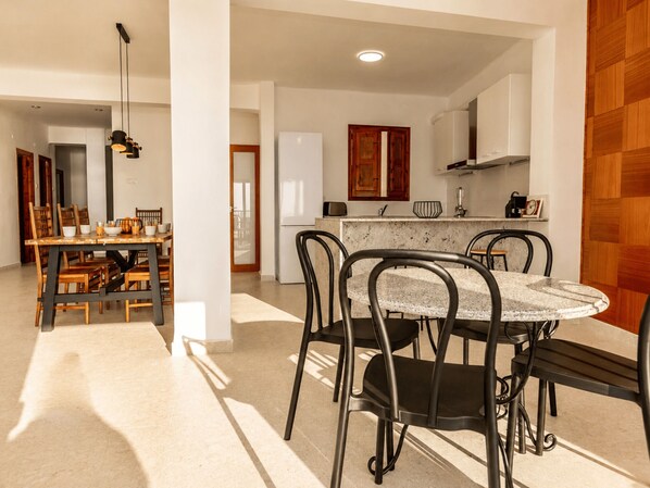 Un coin repas avec une table ronde et des chaises, une cuisine en arrière-plan et un panneau en bois sur la droite.